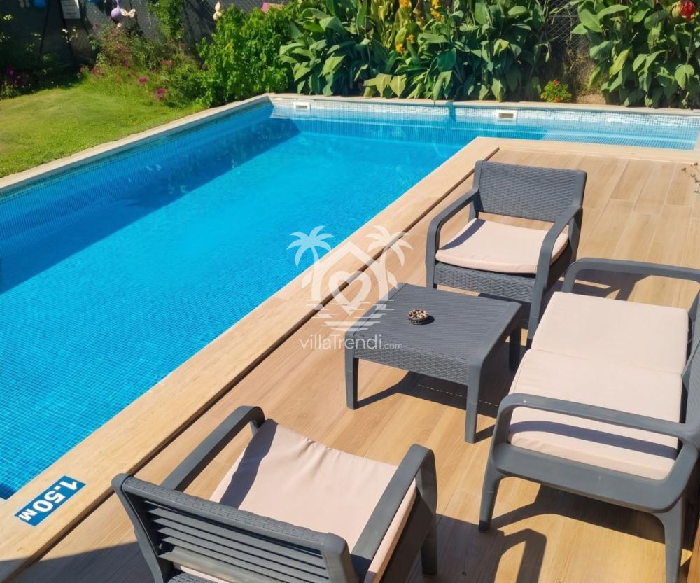 İnlice doğa içinde ahşap tatil evi güneşlenme alanı ve modern şezlonglar.