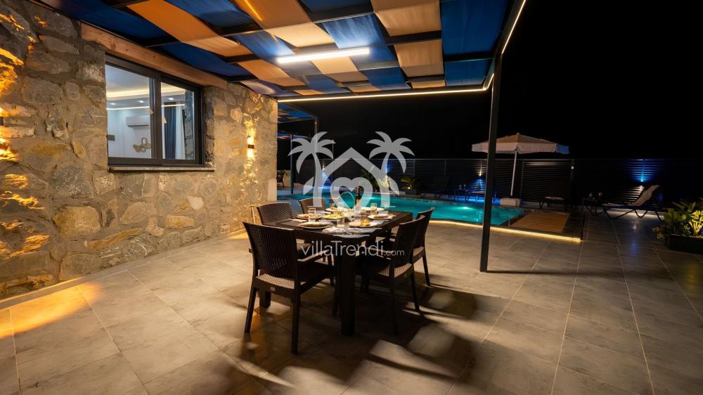 Villa Meyra gece ışıklandırmalı havuz başı ahşap yemek masası.
